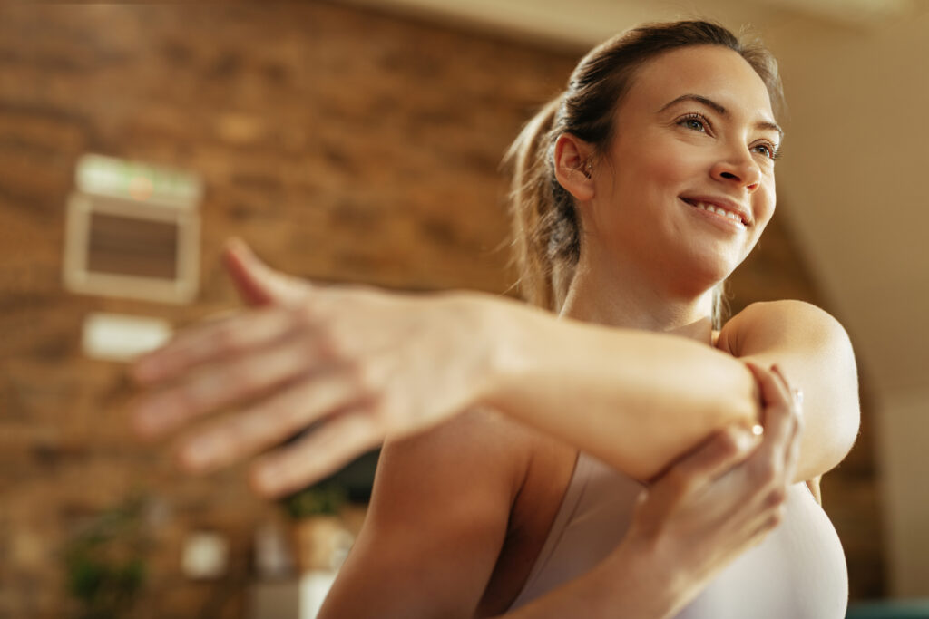 vista-de-angulo-baixo-da-mulher-atletica-feliz-aquecendo-e-esticando-o-braco-em-casa-1024x683 💆‍♀️ Autocuidado: reconectando com o corpo e fortalecendo a autoestima